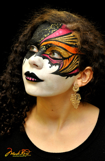woman in a full face mask patinging with the top half in black, gold, and pink while the bottom is white